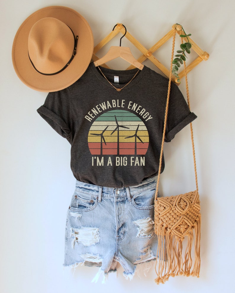 May include: A dark grey t-shirt with a vintage-style graphic of wind turbines in front of a sunset. The text "Renewable Energy I'm a Big Fan" is printed on the shirt.