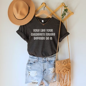 A dark grey heather unisex crew neck short sleeve Bella Canvas t-shirt that says "vote like your children's future depends on it" in white chalkboard font