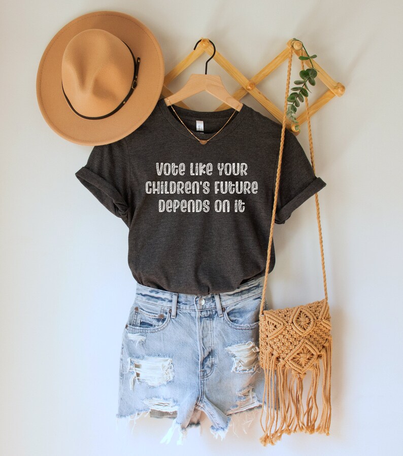 A dark grey heather unisex crew neck short sleeve Bella Canvas t-shirt that says "vote like your children's future depends on it" in white chalkboard font
