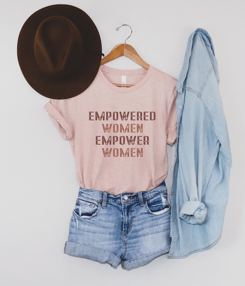 May include: A pink t-shirt with the text "EMPOWERED WOMEN EMPOWER WOMEN" in a gradient of brown and pink.