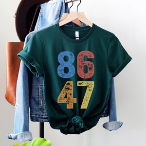 A forest (dark) green unisex crew neck short sleeve Bella+Canvas t-shirt that says "86 47" on the front in large bold distressed numbers, with a blue 8, red 6, orange 4, and yellow 7