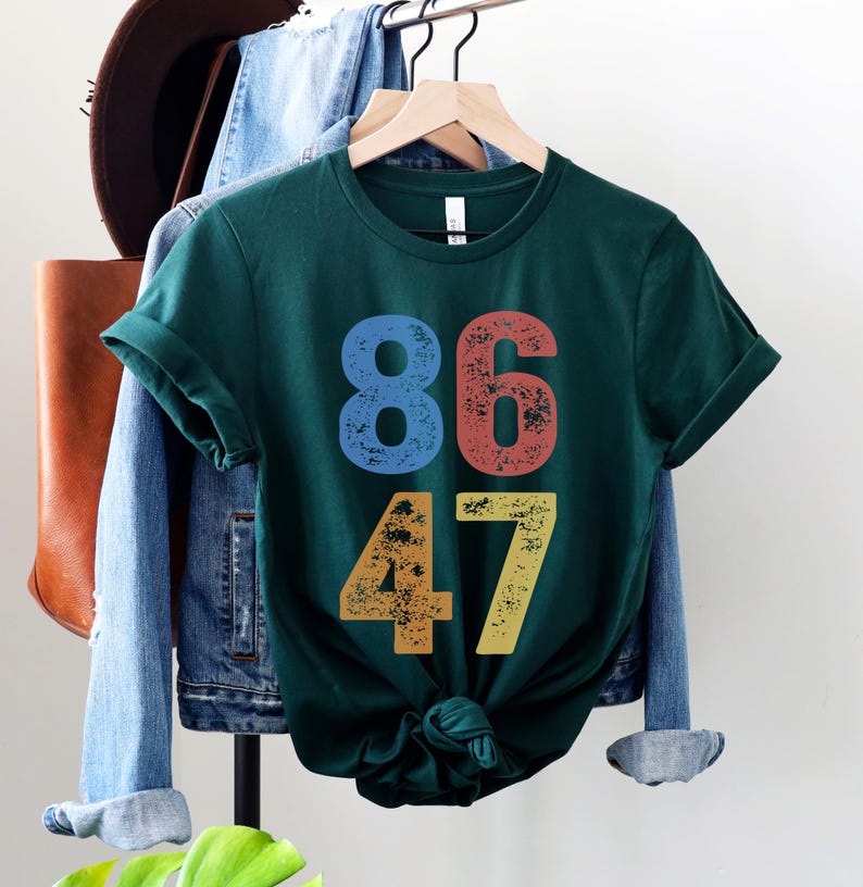 A forest (dark) green unisex crew neck short sleeve Bella+Canvas t-shirt that says "86 47" on the front in large bold distressed numbers, with a blue 8, red 6, orange 4, and yellow 7