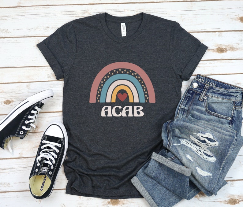 May include: A dark gray t-shirt with a rainbow design and the text "ACAB" in a retro font. The rainbow has a red heart in the center and stars on the outside.