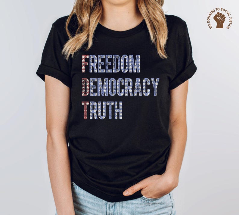A black unisex crew neck short sleeve Bella+Canvas t-shirt that says "FREEDOM DEMOCRACY TRUTH" on the chest in three lines in blue block text with white stars inside the letters. The first letter of each word in in red with white stars, subtly spelling "FDT" down the shirt