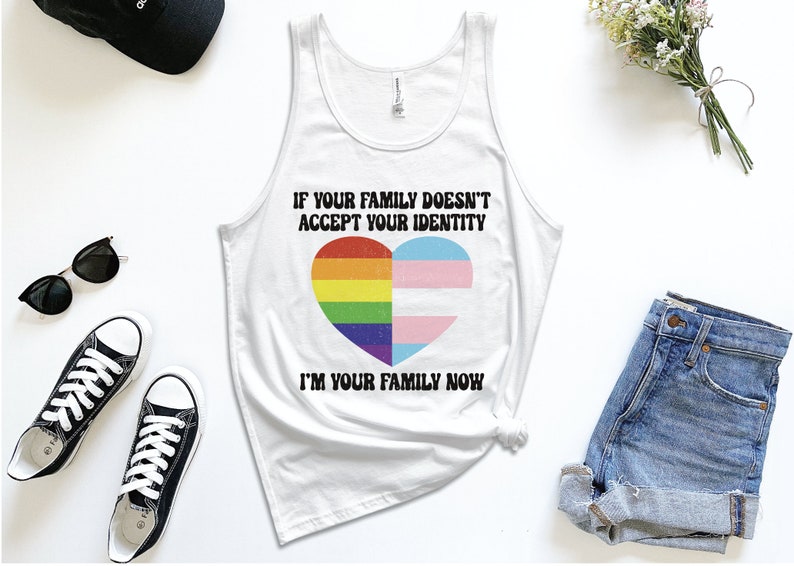 May include: White tank top with a rainbow and transgender pride flag heart design. The text reads "If your family doesn't accept your identity I'm your family now."