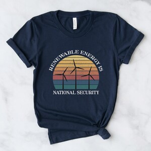 May include: Navy blue t-shirt with a vintage-style graphic of wind turbines in front of a sunset. The text "Renewable Energy is National Security" is printed on the shirt.