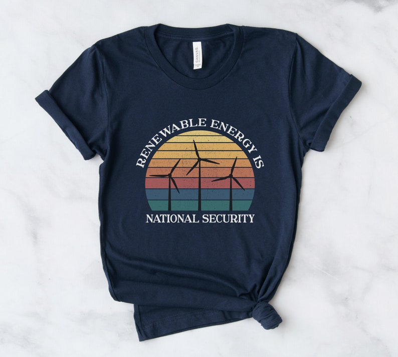 May include: Navy blue t-shirt with a vintage-style graphic of wind turbines in front of a sunset. The text "Renewable Energy is National Security" is printed on the shirt.