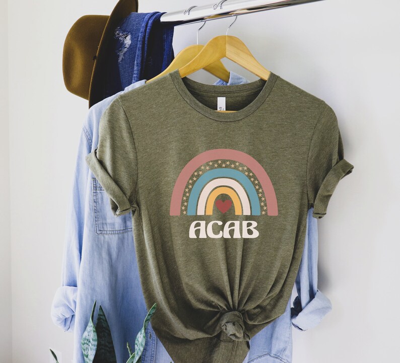 May include: A green t-shirt with a rainbow graphic and the text "ACAB" in a retro font. The rainbow has a red heart in the center.