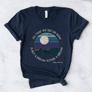 May include: Navy blue t-shirt with a vintage-style graphic of a moon, mountains, and a sunset. The text reads "All that we see or seem is but a dream within a dream - Edgar Allan Poe".