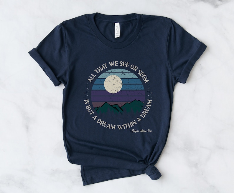 May include: Navy blue t-shirt with a vintage-style graphic of a moon, mountains, and a sunset. The text reads "All that we see or seem is but a dream within a dream - Edgar Allan Poe".