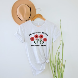 May include: A white t-shirt with a graphic of red flowers and the text "Not Fragile Like A Flower Fragile Like A Bomb".