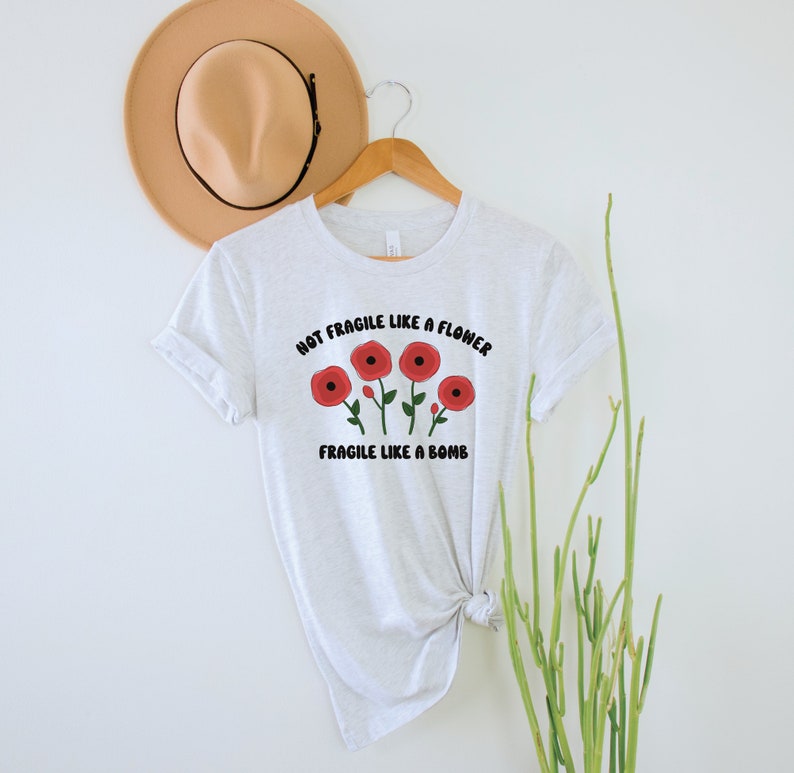 May include: A white t-shirt with a graphic of red flowers and the text "Not Fragile Like A Flower Fragile Like A Bomb".