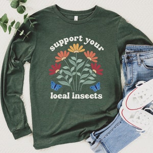 A heather forest green unisex long sleeve crew neck t-shirt with the words "support your local insects" in white text around an image of colorful flowers and butterflies
