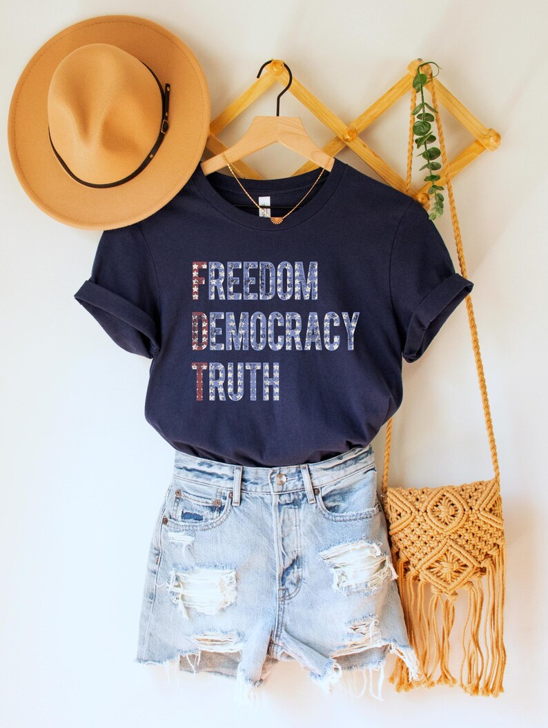 A navy blue unisex crew neck short sleeve Bella+Canvas t-shirt that says "FREEDOM DEMOCRACY TRUTH" on the chest in three lines in blue block text with white stars inside the letters. The first letter of each word in in red with white stars, subtly spelling "FDT" down the shirt