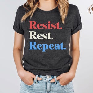 May include: A dark gray t-shirt with the text "Resist. Rest. Repeat." in red, white, and blue.
