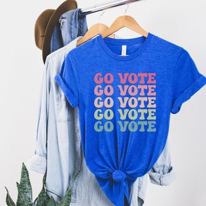 A heather true royal (bright blue) unisex crew neck short sleeve t-shirt that says "go vote" repeating 5 times in pastel colors