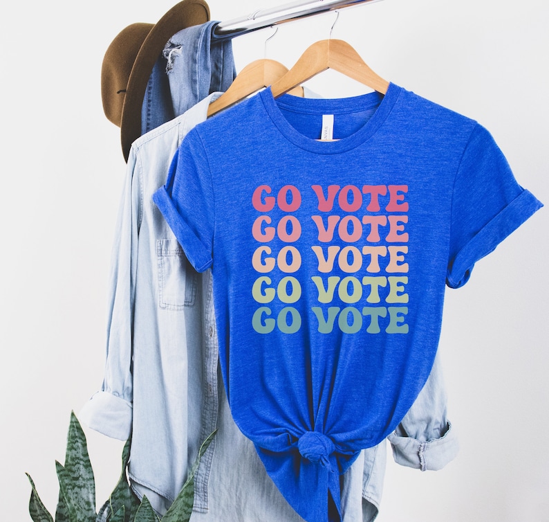 A heather true royal (bright blue) unisex crew neck short sleeve t-shirt that says "go vote" repeating 5 times in pastel colors