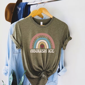 May include: A green t-shirt with a rainbow design and the text "ABOLISH ICE" in white. The rainbow has a red, pink, yellow, blue, and green color scheme with white stars.