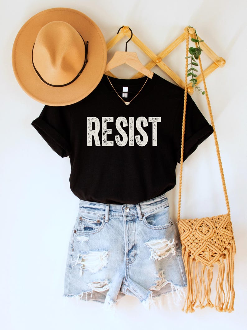 A black unisex crew neck short sleeve Bella+Canvas t-shirt that says "RESIST" in distressed white tall block text