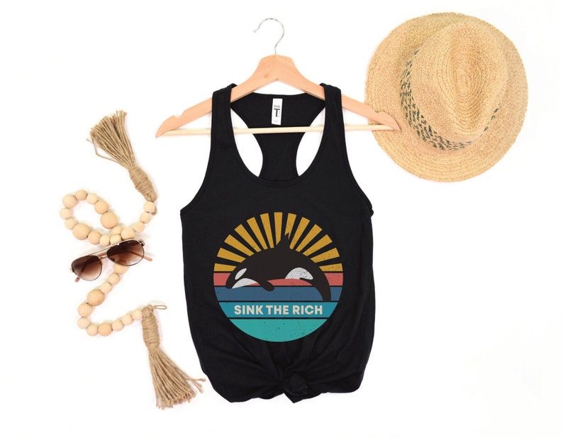 A black women's racerback tank top that says "sink the rich" in white over a retro graphic of an orca whale in the ocean