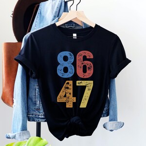A black unisex crew neck short sleeve Bella+Canvas t-shirt that says "86 47" on the front in large bold distressed numbers, with a blue 8, red 6, orange 4, and yellow 7