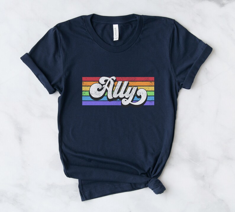 May include: Navy blue t-shirt with a rainbow stripe design and the word "Ally" in a retro font.