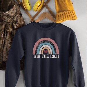 May include: A navy blue sweatshirt with a rainbow graphic and the text "Tax the Rich". The rainbow is made up of pink, blue, yellow, and green stripes with white stars around the edges. A red heart is in the center of the rainbow.