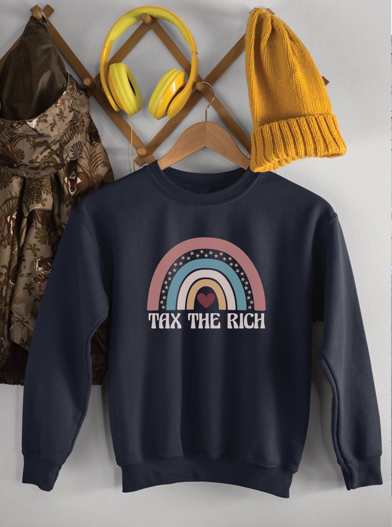 May include: A navy blue sweatshirt with a rainbow graphic and the text "Tax the Rich". The rainbow is made up of pink, blue, yellow, and green stripes with white stars around the edges. A red heart is in the center of the rainbow.
