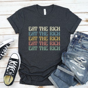 A dark grey heather unisex crew neck short sleeve Bella Canvas t-shirt that says "eat the rich" repeated 5 times in retro font and colors