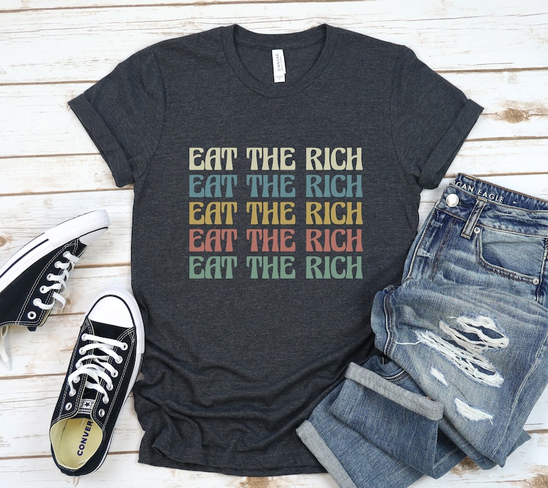 A dark grey heather unisex crew neck short sleeve Bella Canvas t-shirt that says "eat the rich" repeated 5 times in retro font and colors