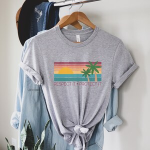 May include: Gray t-shirt with a retro sunset and palm trees graphic. The text "Respect It. Protect It." is printed below the graphic.