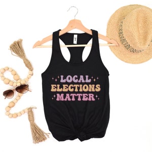 A black women’s racerback tank top that says "local elections matter" in purple, yellow, and pink retro text with retro stars