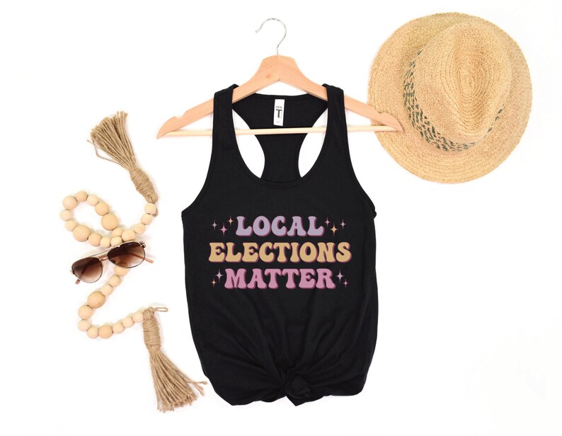 A black women’s racerback tank top that says "local elections matter" in purple, yellow, and pink retro text with retro stars