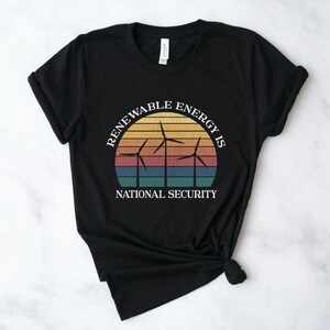 May include: Black t-shirt with a vintage-style graphic of wind turbines and a sunset. The text reads "Renewable Energy is National Security."