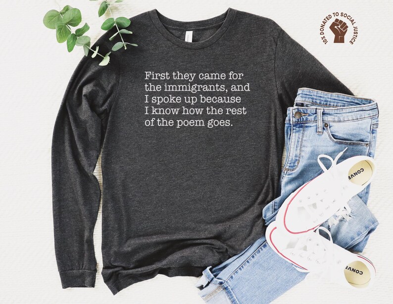 A dark grey heather unisex long sleeve crew neck t-shirt that says "First they came for the immigrants, and I spoke up because I know how the rest of the poem goes." in white typewriter font on the chest.