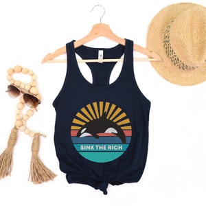 A navy blue women's racerback tank top that says "sink the rich" in white over a retro graphic of an orca whale in the ocean