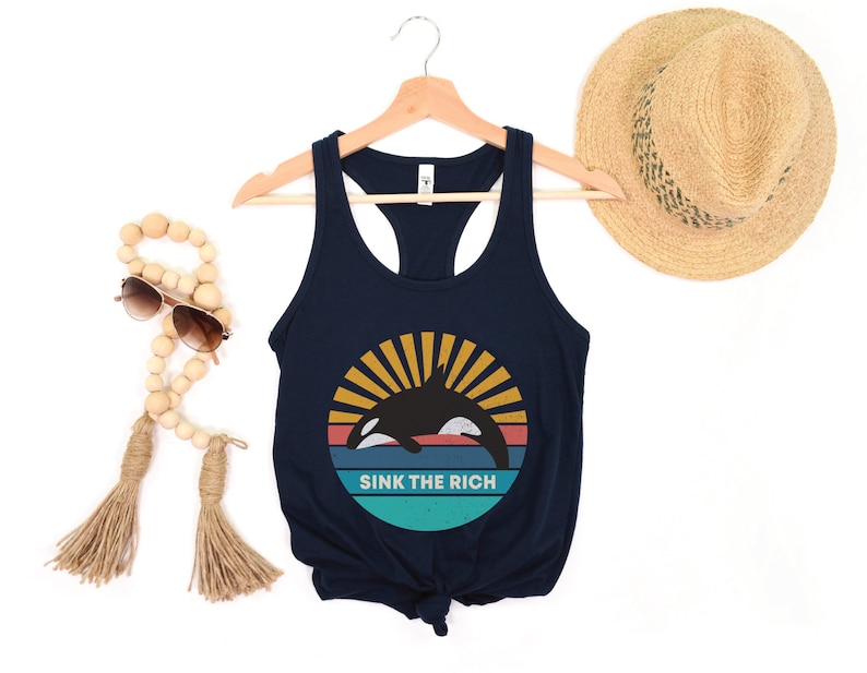 A navy blue women's racerback tank top that says "sink the rich" in white over a retro graphic of an orca whale in the ocean
