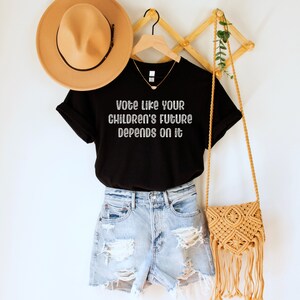 A black unisex crew neck short sleeve Bella Canvas t-shirt that says "vote like your children's future depends on it" in white chalkboard font
