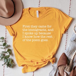 A gold (dark yellow) unisex short sleeve crew neck t-shirt that says "First they came for the immigrants, and I spoke up because I know how the rest of the poem goes." in white typewriter font on the chest.