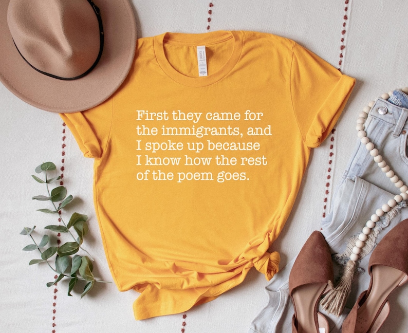 A gold (dark yellow) unisex short sleeve crew neck t-shirt that says "First they came for the immigrants, and I spoke up because I know how the rest of the poem goes." in white typewriter font on the chest.