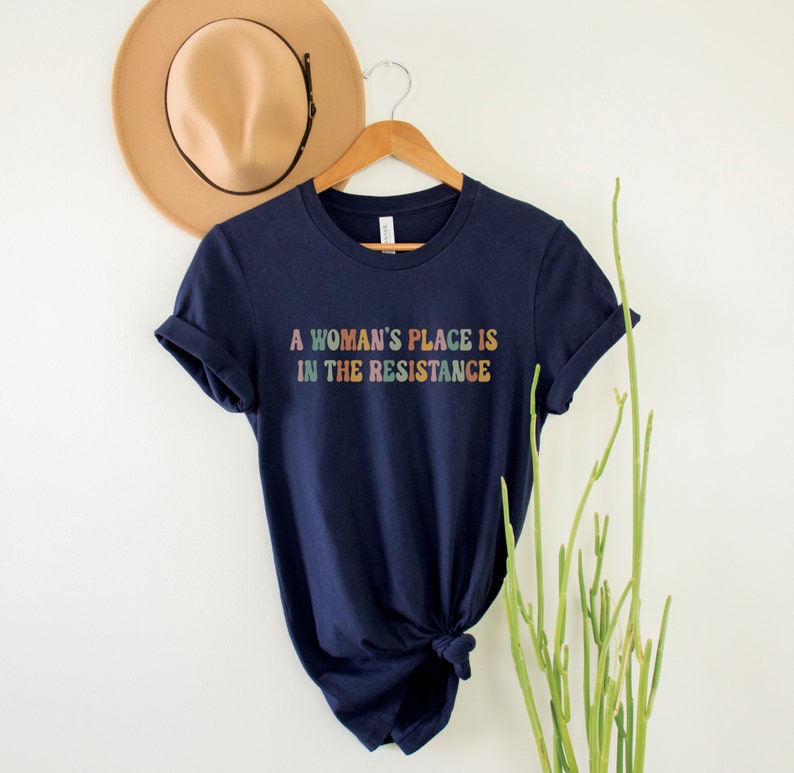 May include: A navy blue t-shirt with the text "A woman's place is in the resistance" printed in rainbow colours.