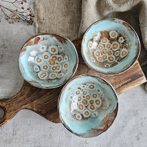 K&ouml;nnte beinhalten: Drei kleine Keramikschalen mit hellblauer Glasur und braunem, gesprenkeltem Muster. Die Schalen sind auf einem Holztablett angeordnet.