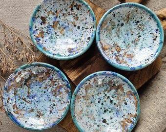 May include: Set of four small ceramic bowls with a speckled blue, white and gold glaze. The bowls have a slightly rounded shape and a turquoise rim.