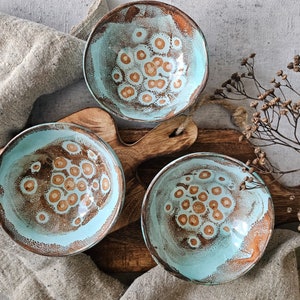 K&ouml;nnte beinhalten: Drei tealblaue Keramikschalen mit braunem, gesprenkeltem Design. Die Schalen sind auf einer Holzoberfl&auml;che angeordnet.