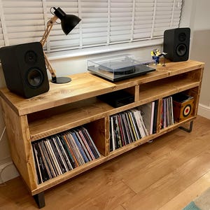 May include: A wooden record player stand with shelves for vinyl records. The stand has a turntable on top and two black speakers on the sides. The stand is made of reclaimed wood and has a rustic look.