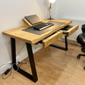 May include: A wooden desk with black metal legs and two drawers. The desk has a laptop, keyboard, and mouse on top. The desk is in a room with a white wall and a black office chair.