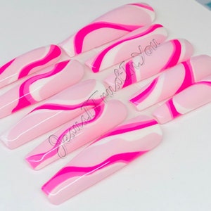 May include: Set of ten long, pink and white swirl-patterned fake nails. The nails are long and narrow, with a pointed tip. The swirl pattern is created with pink and white paint, and the nails have a glossy finish.