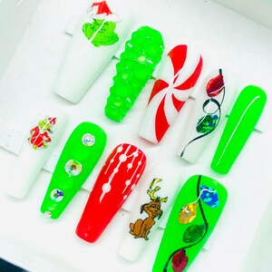 May include: Set of ten green and white Christmas-themed nail tips. The tips feature designs such as a candy cane, a Grinch, Christmas lights, and a reindeer.