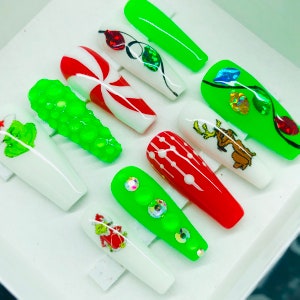 May include: Set of ten green and white Christmas-themed press-on nails. The nails feature designs such as candy canes, Christmas lights, a Grinch, a reindeer, and green glitter.