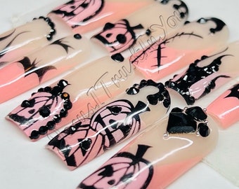 May include: Set of pink and black Halloween-themed press-on nails with pumpkin and bat designs. The nails are decorated with black rhinestones.